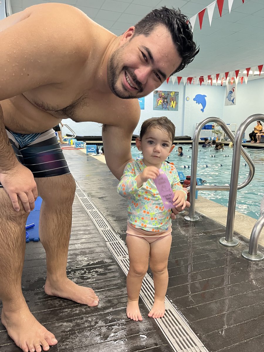 Francesca as a toddler at the pool, holding her first level-up ribbon