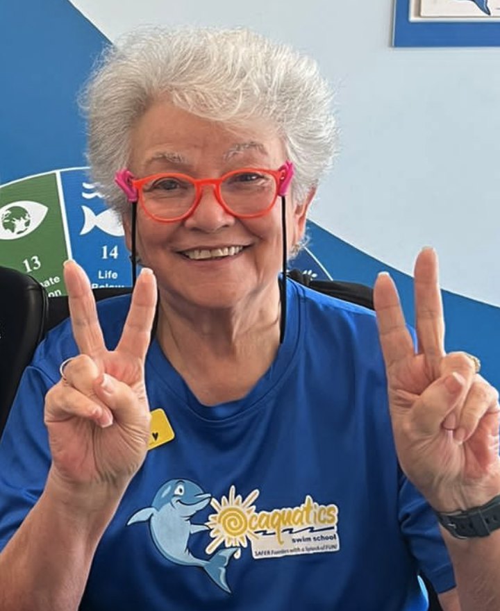 Ms. Lucy smiling in an Ocaquatics shirt, holding up two peace signs